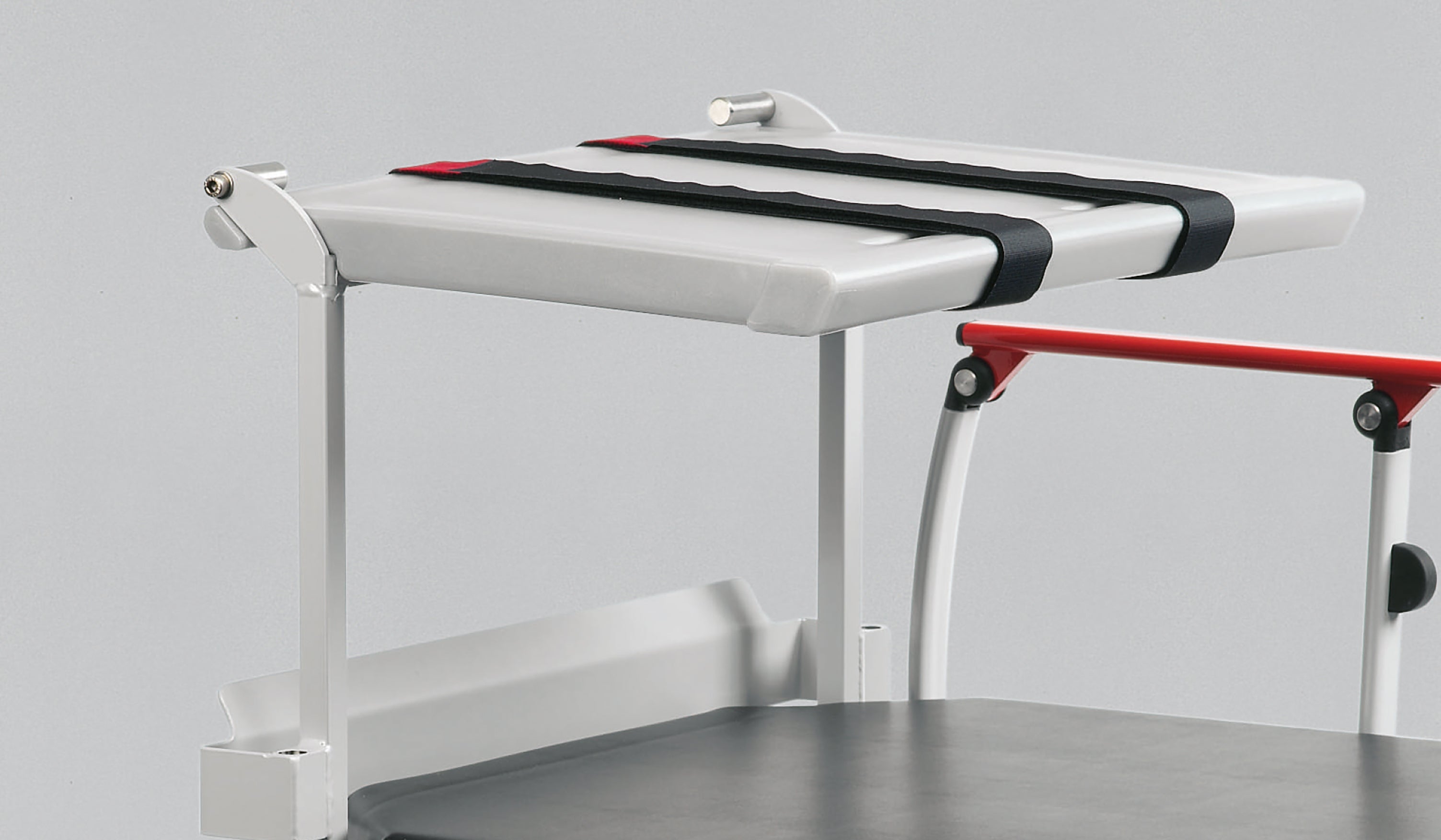 White and red examination table with black straps on a gray background