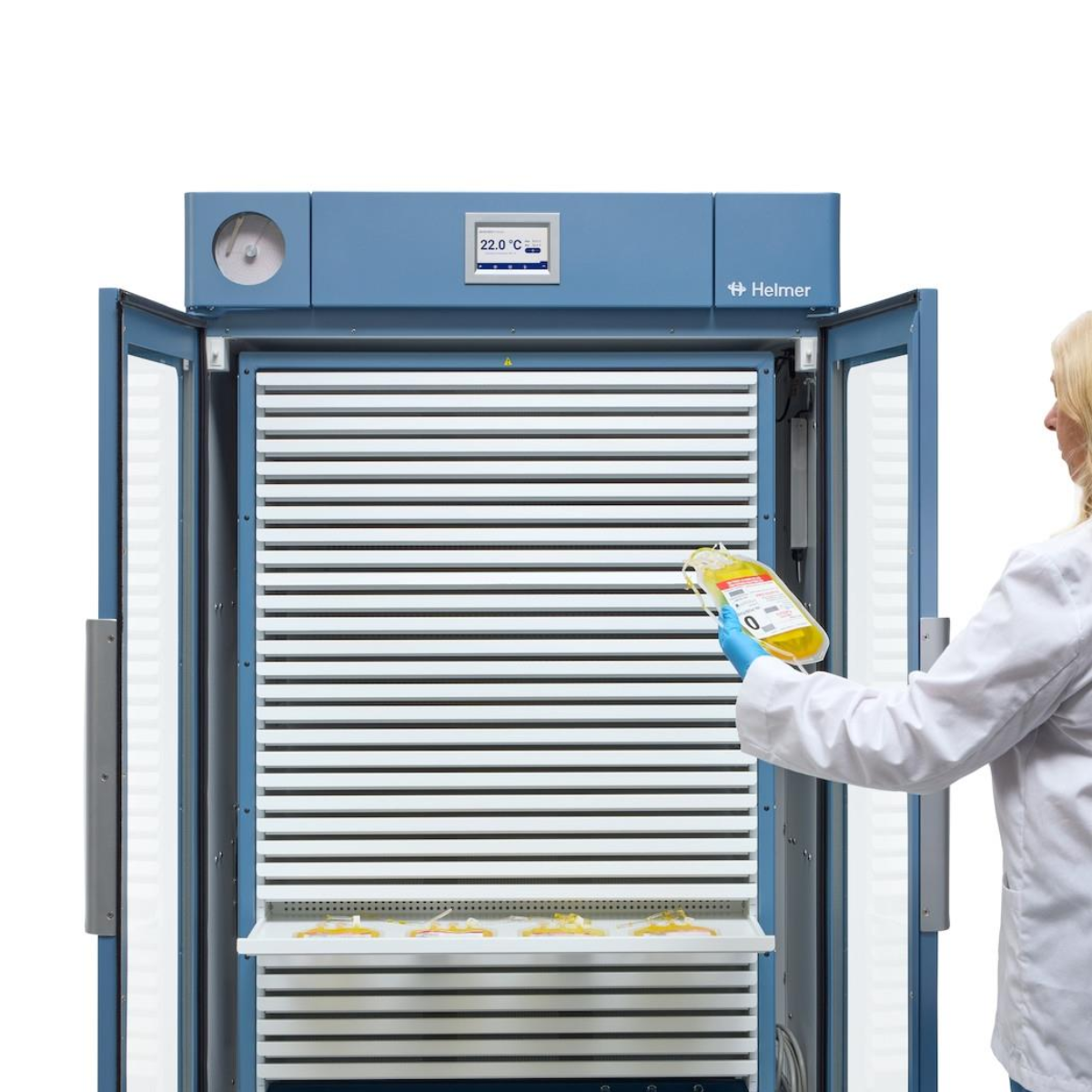 Person in a lab coat opening a large blue refrigerator holding a yellow container. PC4200 Pro Line floor-standing platelet incubator with built-in agitator, Helmer Scientific unit for high-capacity platelet storage with precise temperature control and gentle agitation.
